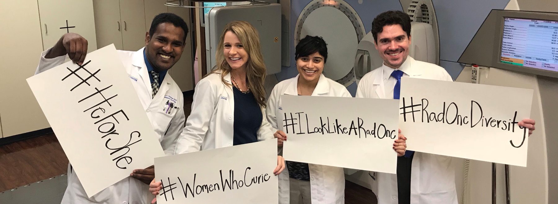 Four radiation oncologists hold signs stating HeForShe, WomenWhoCurie, ILookLikeARadOnc and RadOncDiversity